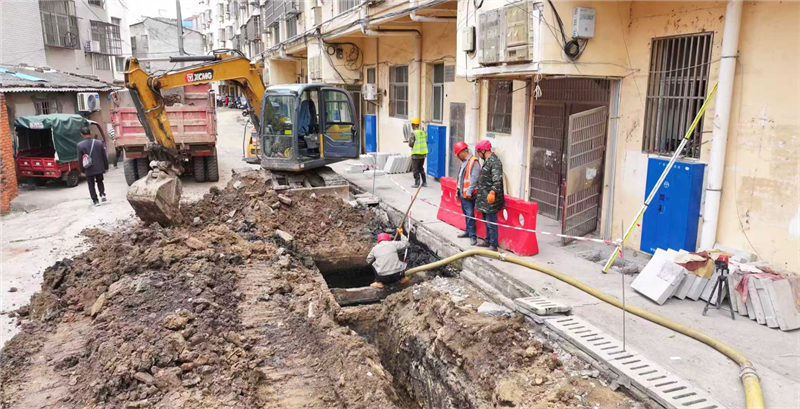 老旧小区改造现场，挖掘机轰鸣作业，有序开挖路面铺设地下管网。
